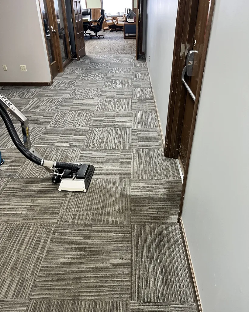 Professional hot water steam extraction carpet cleaning machine running on patterned office carpet tiles.