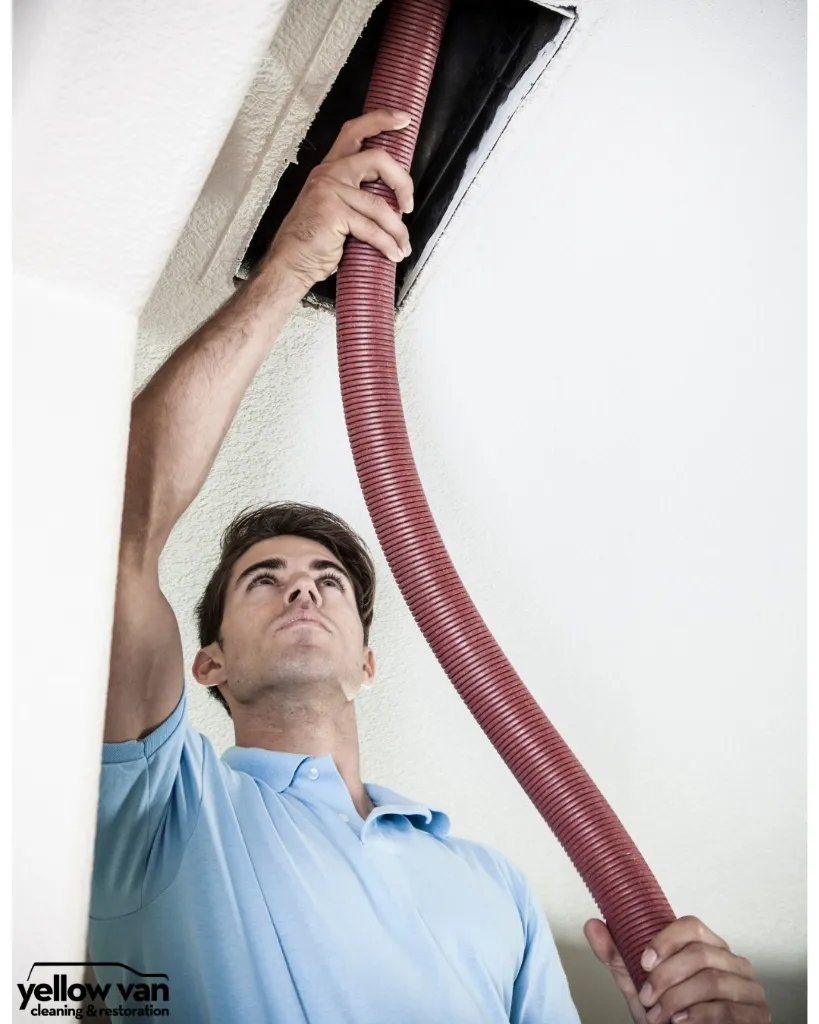 Professional HVAC technician cleaning an air duct register in a ceiling using high-suction negative-air equipment.